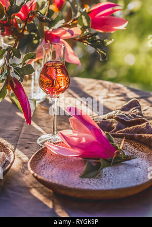 Beautiful table setting in garden on sunset light. Table decorated with magnolia flowers under magnolia tree. Stock Photo