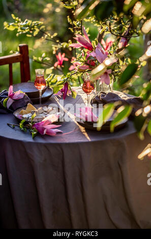 Beautiful table setting in garden on sunset light. Table decorated with magnolia flowers under magnolia tree. Stock Photo