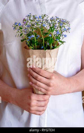 A bouquet of forget-me-nots in the hands of the girl, close-up. Woman holding a bouquet with Forget-me-not flowers. The idea of spring clearance. Stock Photo