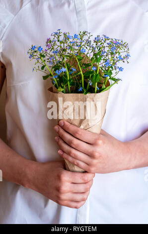 A bouquet of forget-me-nots in the hands of the girl, close-up. Woman holding a bouquet with Forget-me-not flowers. The idea of spring clearance. Stock Photo