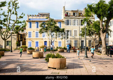Children play football between flower boxes at the heart of the historic district of Le Panier in Marseille, France, while elders chat together. Stock Photo