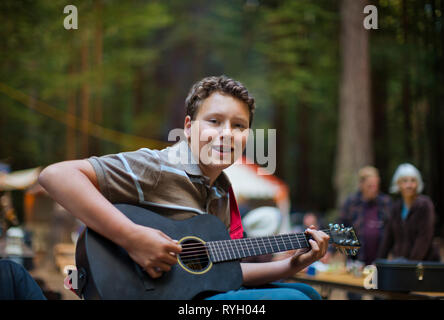 Portrait of boy smiling as he plays an acoustic guitar in an outdoor location. Stock Photo