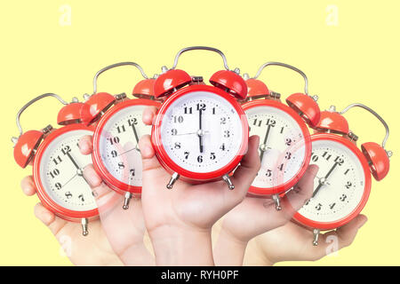 many red alarm clocks in hand, on a yellow background, concept time to get up Stock Photo