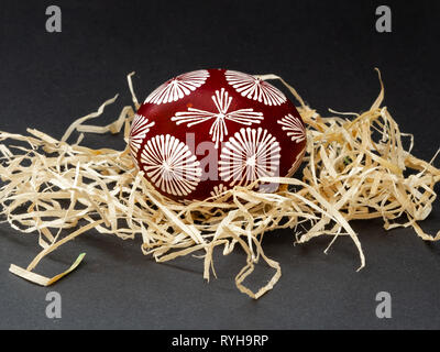 One traditional lithuanian Easter egg natural painted dark red and white in geometric ornament with bees wax in the nest, on black background Stock Photo