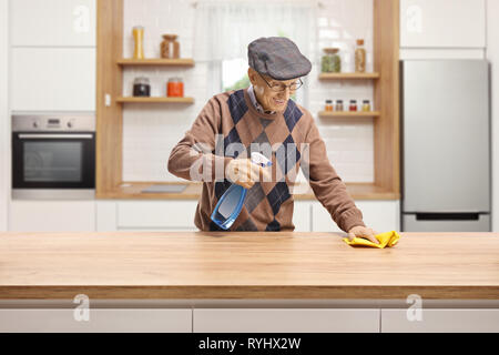 Elderly man cleaning a wooden counter in a kitchen Stock Photo