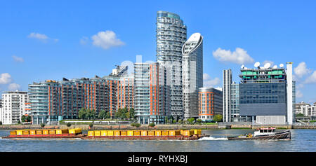 River Thames tug boat & barge containers full of London waste rubbish towed down river for recycling modern apartment building Poplar East London UK Stock Photo