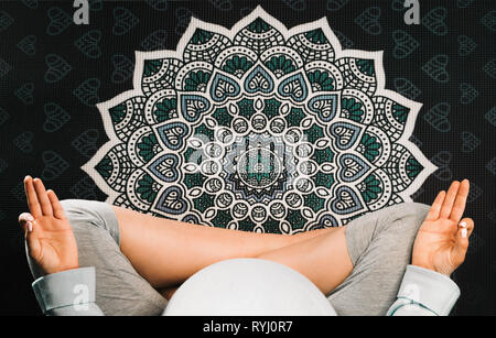 Pregnant woman sitting in lotus position on mandala yoga mat and meditating. Top view Stock Photo
