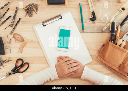 Female carpenter using smartphone, mock up screen top view of woodwork carpentry workshop desk Stock Photo