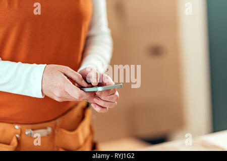 Female carpenter is using mobile phone for text messaging, close up of hands typing sms on smartphone touch screen, selective focus Stock Photo