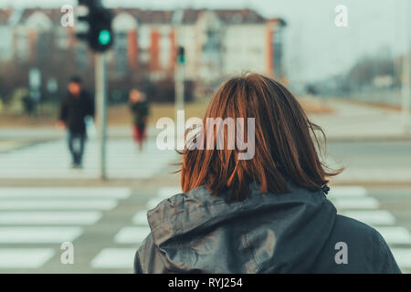 Rear view of woman on city street pedestrian crossing in cold winter afternoon Stock Photo