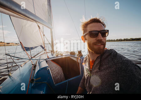 young european man standing at edge of yacht looking at sea. Travelling on old boat with sail. Luxury lifestyle Stock Photo