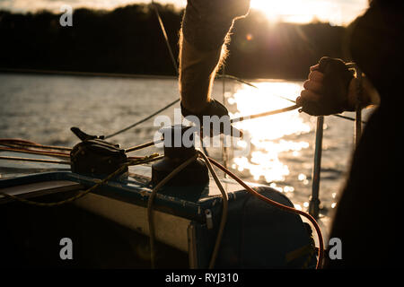 Silhouette of a sailors hands on a winch rope on a sailboat on a sunset. Shot with a selective focus Stock Photo