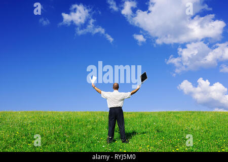 Businessman standing on green field, blue sky and white clouds in background Stock Photo