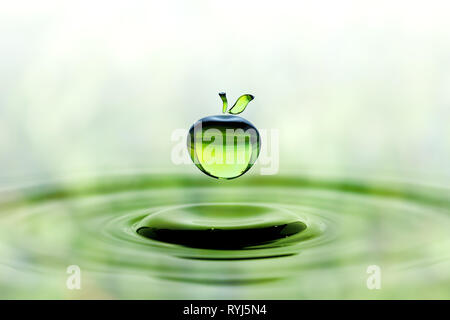 Rain drop in shape of green apple falling on blue water surface. Green blurred pattern in background. Stock Photo