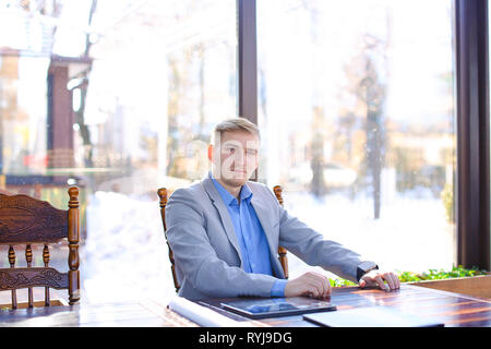 Interior designer using smart watch at cafe with tablet and roll project on table. Young handsome man waiting for business meeting. Concept of enhanci Stock Photo