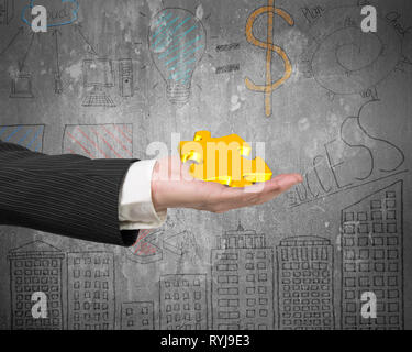 Hand showing gold jigsaw puzzle piece with business concept doodles wall background Stock Photo