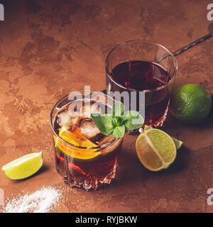 Cocktail of rum and cola ice cubes and lime in glass goblets on a dark brown background. Strong alcoholic drink. Stock Photo