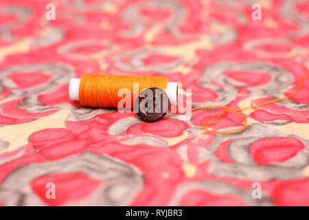 Picture of orange thread with button. Isolated on the colorful background. Stock Photo