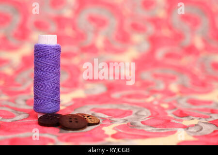 Portrait of purple sewing thread and four button. Isolated on the colorful background. Stock Photo