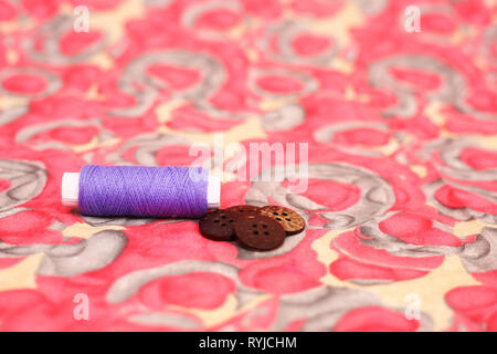 Picture of purple sewing thread and four button. Isolated on the colorful background. Stock Photo