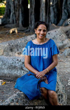 Smiling woman sitting on a tree in a park in Palermo, Sicily (Italy). Stock Photo