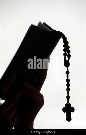 Silhouette of a christian woman reading the bible with prayer beads.  Vietnam.