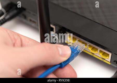 Man plugs internet cable into the router. Ethernet connection concept Stock Photo