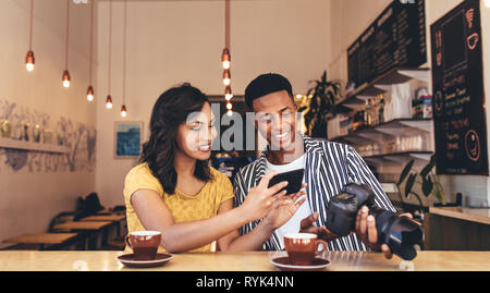 Young woman taking pictures from male friends digital camera. Young man and woman sitting at coffee shop with smart phone and dslr camera.