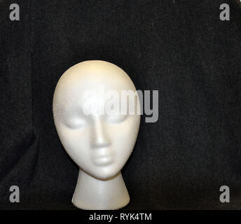 A White Styrofoam Head in front of a Charcoal Fabric Background Stock Photo