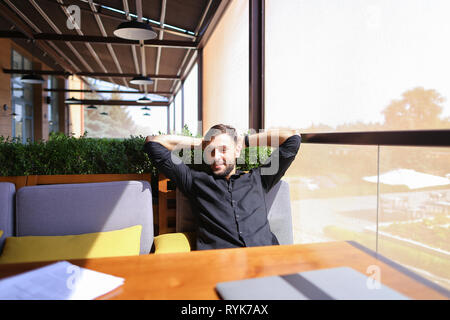 European translator sorting papers and closing laptop lid at cafe. Young persistent man dressed in black shirt looks happy and successful. Concept of  Stock Photo