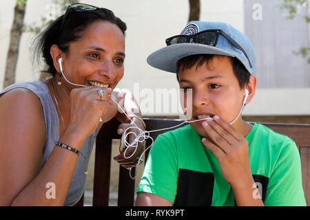 Mother and son having a cell phone conversation and sharing earphones in Sicily (Italy). Stock Photo