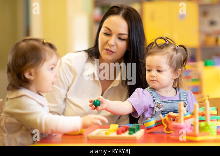 Nursery babies group playing with teacher in daycare centre playroom Stock Photo