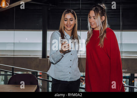 Two women having fun at the cafe and looking at smart phone. Woman showing something to her friend. - Image Stock Photo