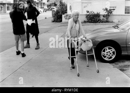 South Beach Miami, Florida USA 1999.  Old woman with zimmer frame walking past an Afro America man who is dressed as a super hero. He is wearing his under shorts over his black costume while being filmed. 1990s US HOMER SYKES. Stock Photo