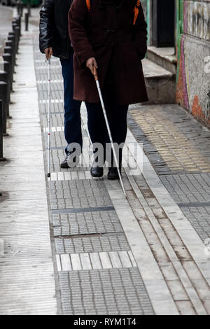 blind man and woman walking on the street using a white walking stick Stock Photo