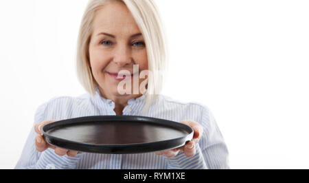 Kitchen woman waitress gives empty black plate for your advertising products isolated on white background. Mock up for use Stock Photo