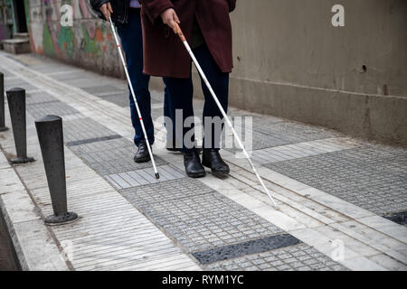 blind man and woman walking on the street using a white walking stick Stock Photo