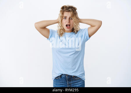 Concerned and worried cute young woman being in trouble, panicking shouting from despair as holding hands on head in worry and anxiety widen eyes Stock Photo