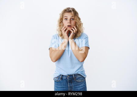Portrait of concerned and worried woman raising eyebrows and open mouth from shock and scare holding hands near lips standing in stupor from Stock Photo