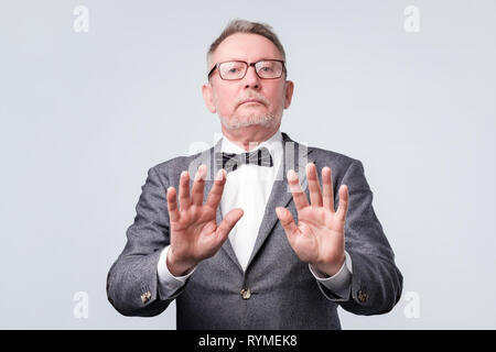 Senior man in suit and glasses showing stop sign against white background Stock Photo