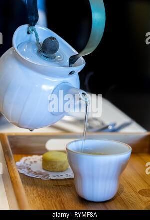 White tea pot pouring onto ceramic cup. Tea setting. Stock Photo