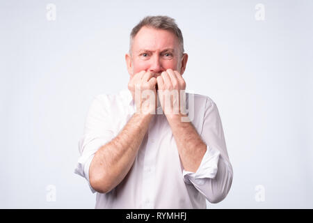 Senior man in white shirt biting nails in fear Stock Photo