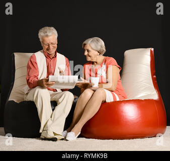 Portrait of elderly couple sitting on armchairs on dark background Stock Photo