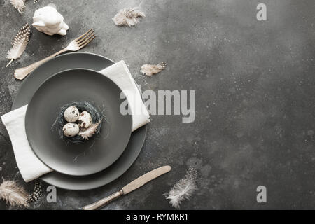 Easter table setting with eggs nest as decor on dark. Top view. Stock Photo