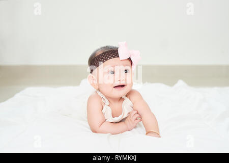 A baby girl is crawling along the floor with an inquisitive look on her face. Horizontal shot. Stock Photo