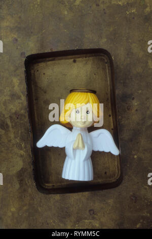 Plastic model of modern angel with hands clasped in prayer lying in tarnished brass box Stock Photo