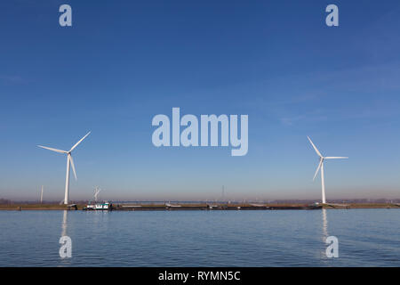 Wind mill, with several wind turbines, near a river, producing green energy in the netherlands Stock Photo