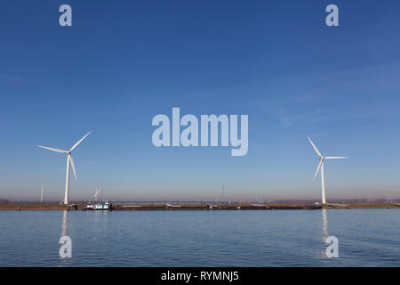 Wind mill, with several wind turbines, near a river, producing green energy in the netherlands Stock Photo