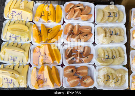 Fruit chunks (mango, green and ripe, sapodilla, a citrus) on plates with the price 20 000 dongs (0.9 USD) on a stall of a street vendor in Saigon. Stock Photo