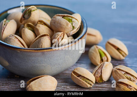 close up color picture of pistachios roasted and salted in a ceramic bowl on a wooden surface Stock Photo